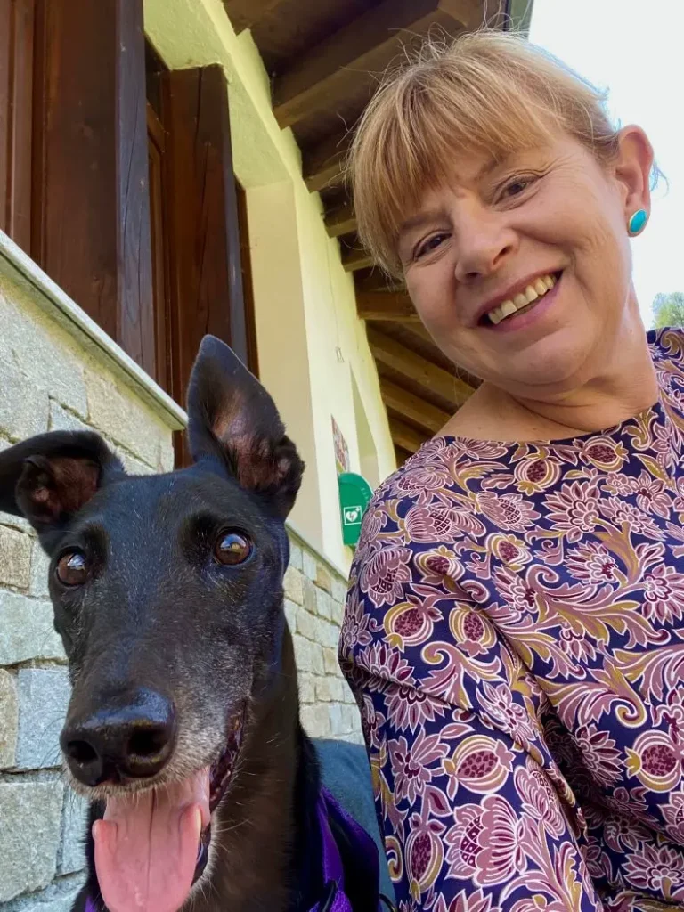 Elena con camicetta a fiori su sfondo bleu, e Lady, con la lingua fuori, in primo piano, accanto a un muro giallo