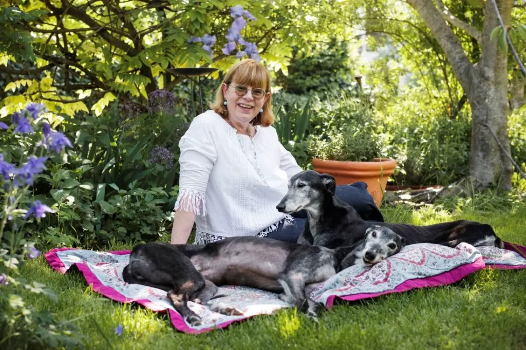Elena e si suoi levrieri anziani, neri, nel giardino fiorito