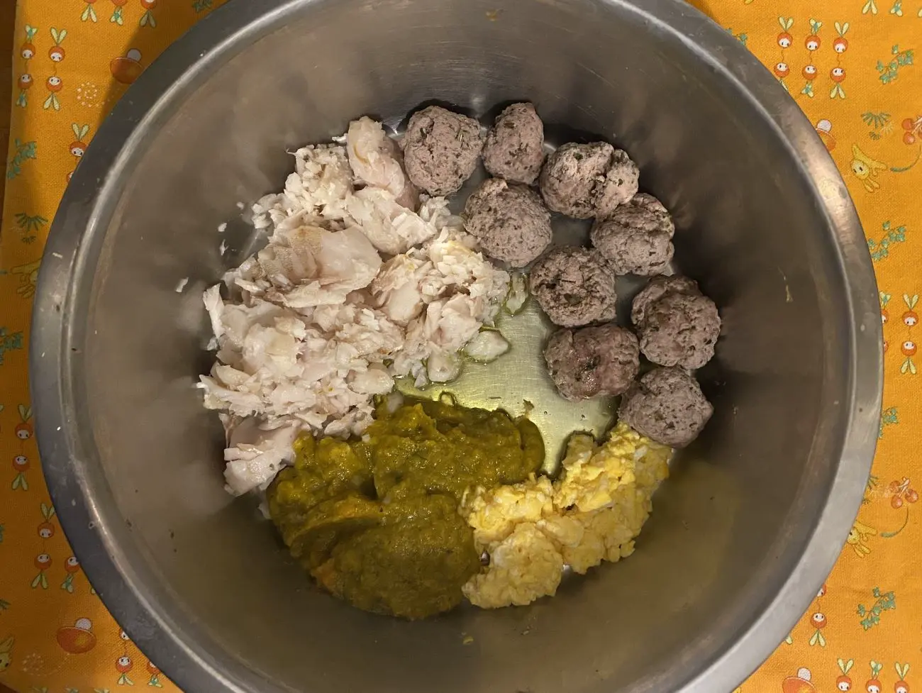 Ciotola in alluminio cn pesce, polpette, uova e verdure. Su tovaglietta arancio
