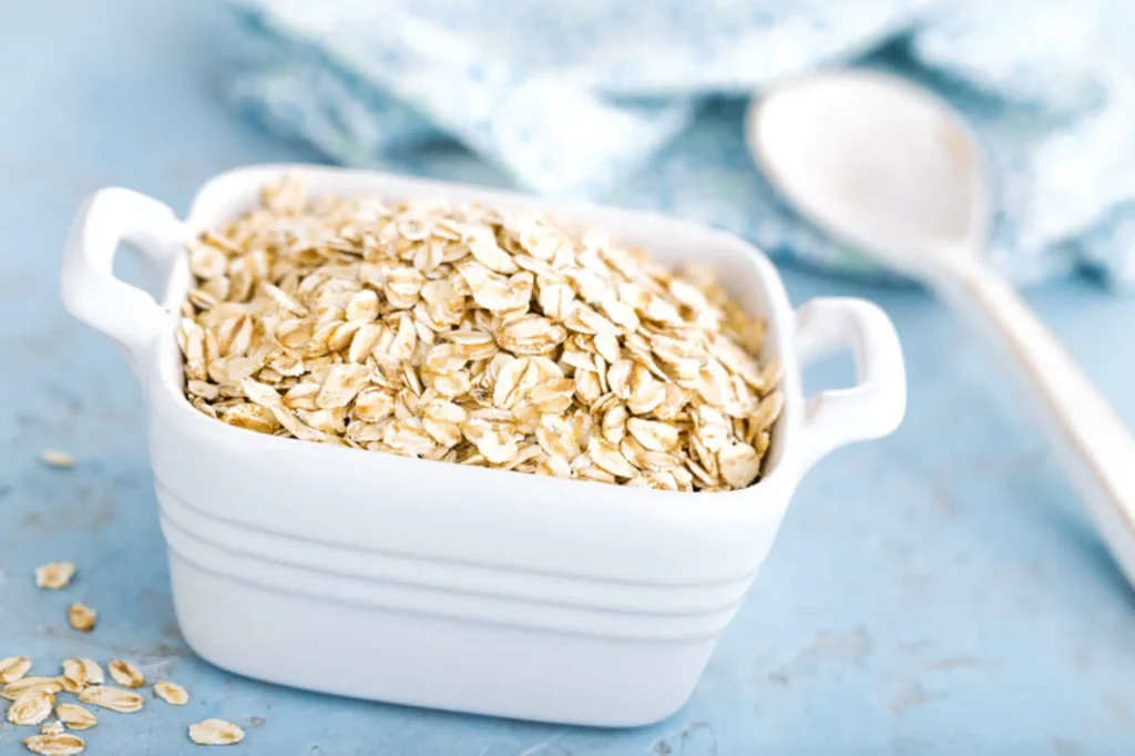 Ciotola quadrata in ceramica bianca, con fiocchi di avena. Su una tovaglia azzurra, sullo sfondo un piatto bianco