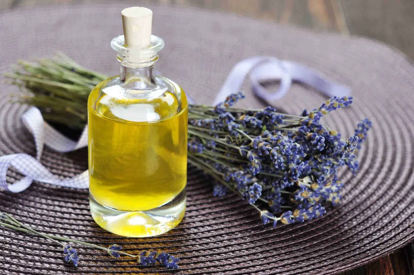 Boccetto di olio essenziale di lavanda, accanto un mazzo di landa essiccata su stuoia del colore dei fiori di lavanda