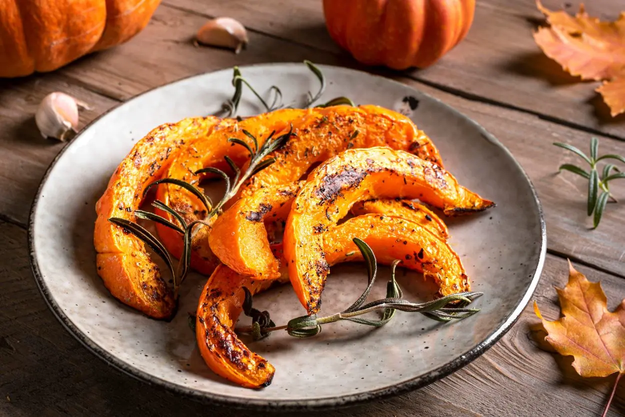 Piatto grigio con fette di zucca arrostite su tavolo in legno