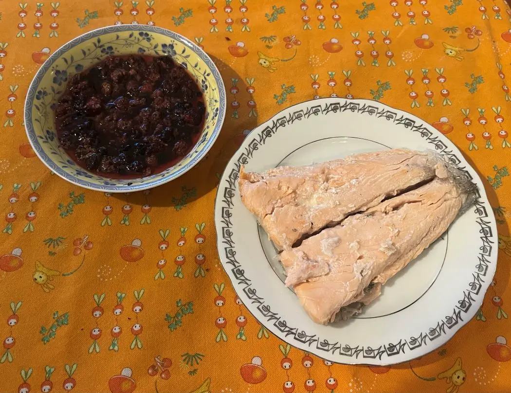 trancio di salmone su piatto bianco e ciotola gialla con frutti di bosco