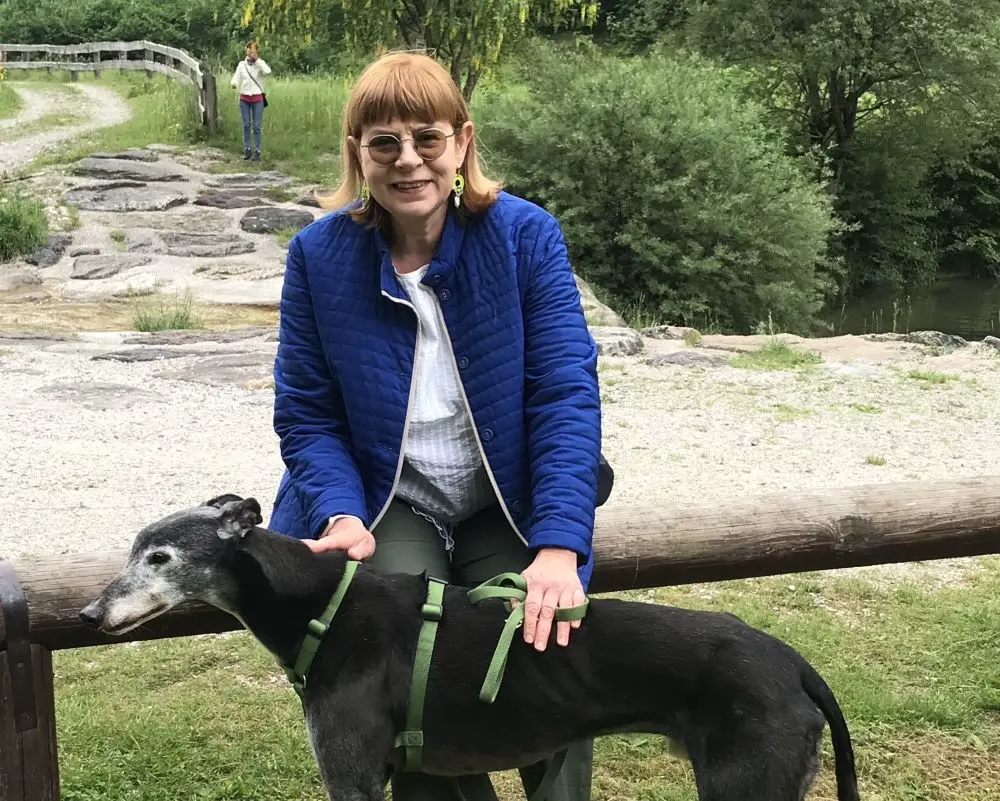 Elena con giacca blu e Rory co, levriero nero, sullo sfondo di un sentiero di montagna
