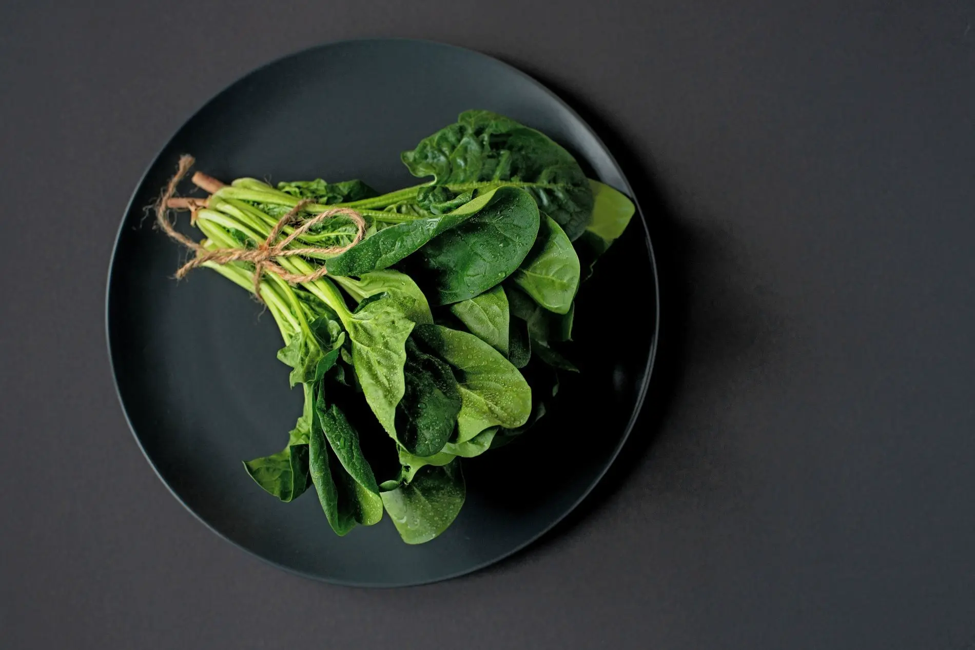 un mazzo di spinaci, legati con un cordino, su un piatto nero, adagiato su un tavolo grigio ardesia