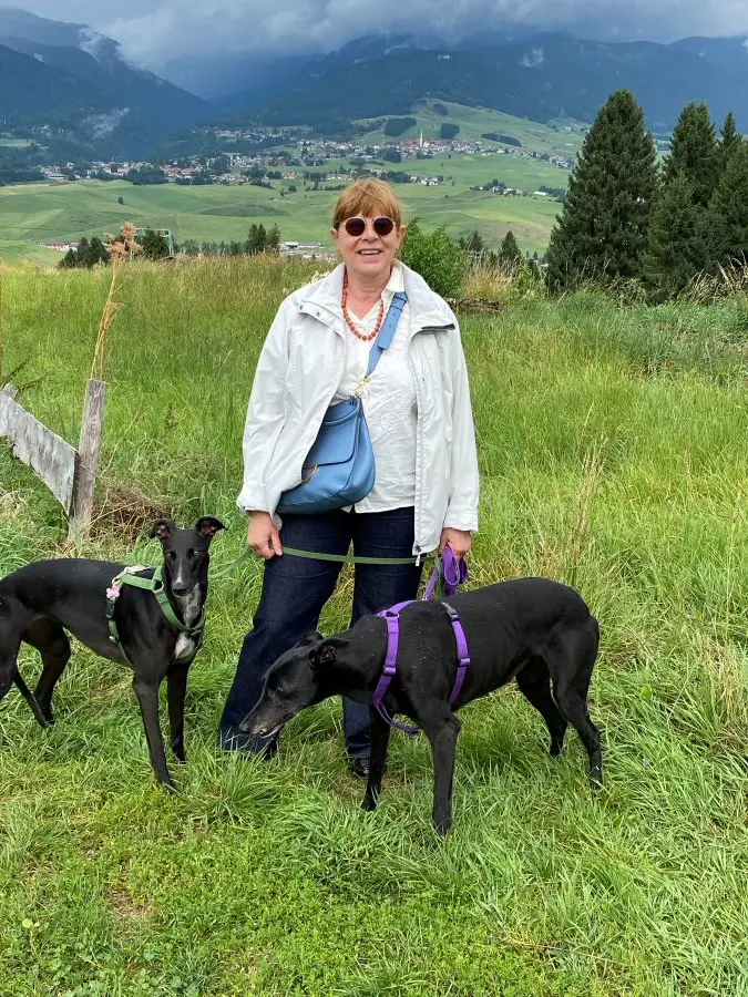 Elena in giacca impermeabile bianca, le sue due levriere nere sullo sfondo labeti e prati verdi
